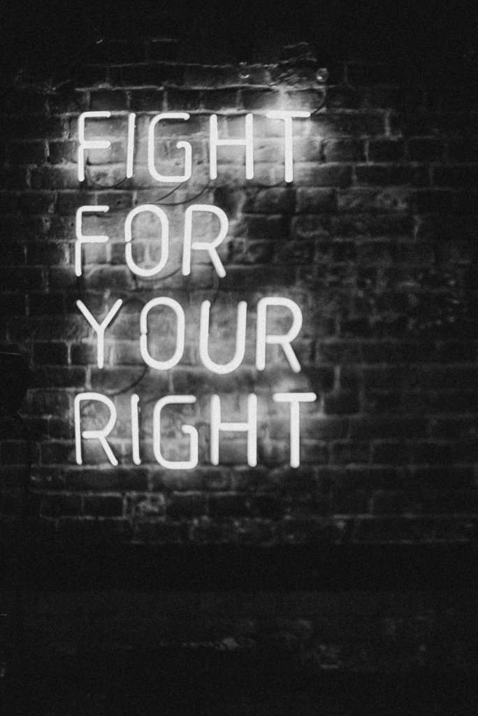 Fight for your right - weiße Neonröhren/ Buchstaben vor schwarzer Wand.